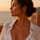 Collier torque rigide en or jaune 18 carats porté ouvert à l'arrière par une femme de profil habillée en blanc au crépuscule.