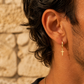Gros plan sur une oreille d'homme portant des créoles de 9 mm avec croix pendantes en or jaune 18 carats, style rock-chic et solaire.