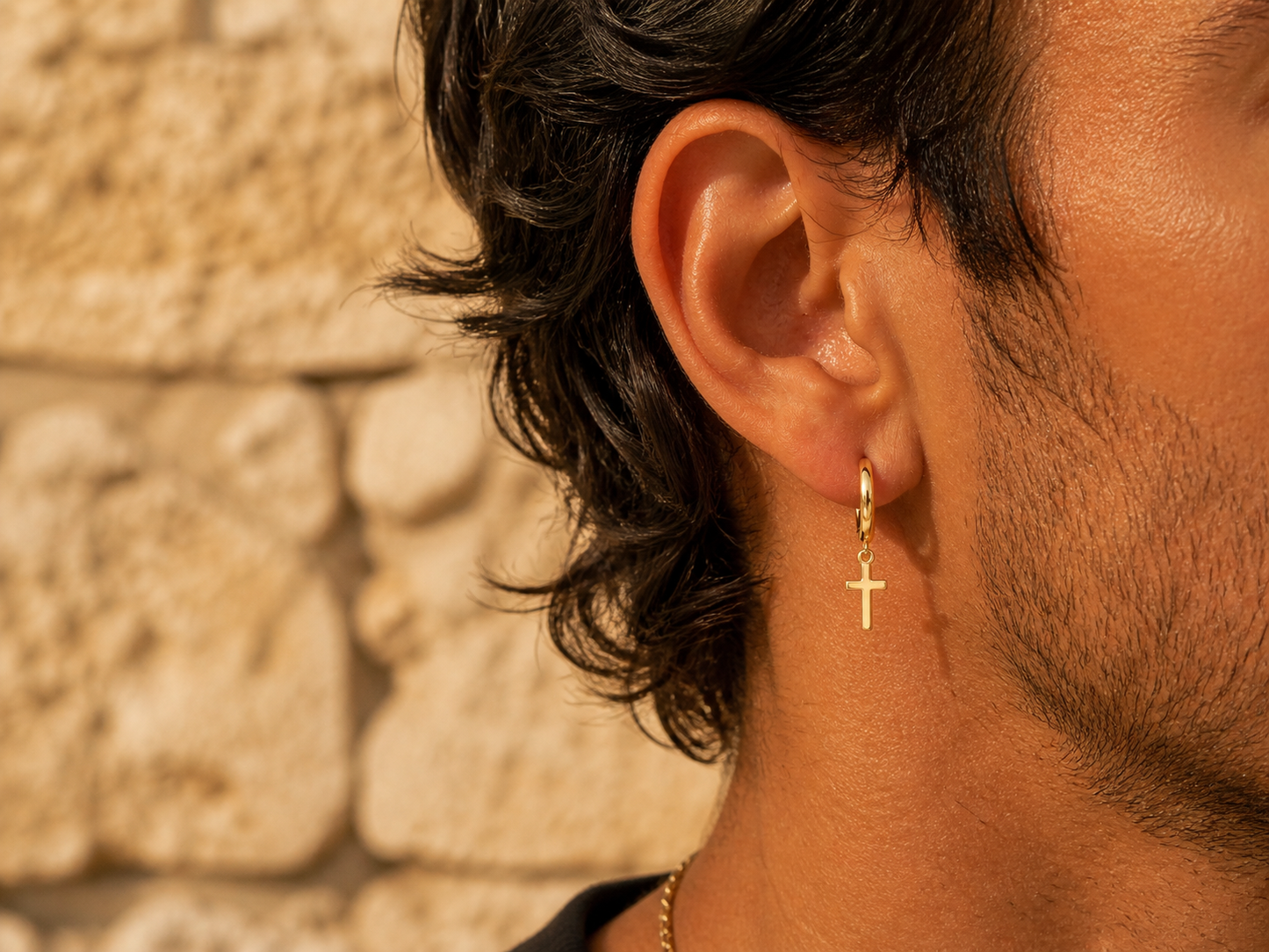 Gros plan sur une oreille d'homme portant des créoles de 9 mm avec croix pendantes en or jaune 18 carats, style rock-chic et solaire.