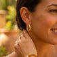 Gros plan sur une femme portant des créoles épaisses en or jaune 18 carats, boucles d'oreilles volumineuses et lumineuses au style solaire.