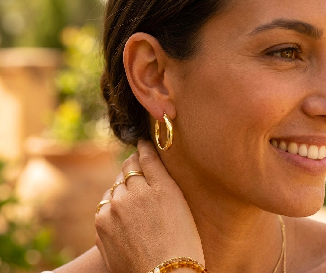 Gros plan sur une femme portant des créoles épaisses en or jaune 18 carats, boucles d'oreilles volumineuses et lumineuses au style solaire.