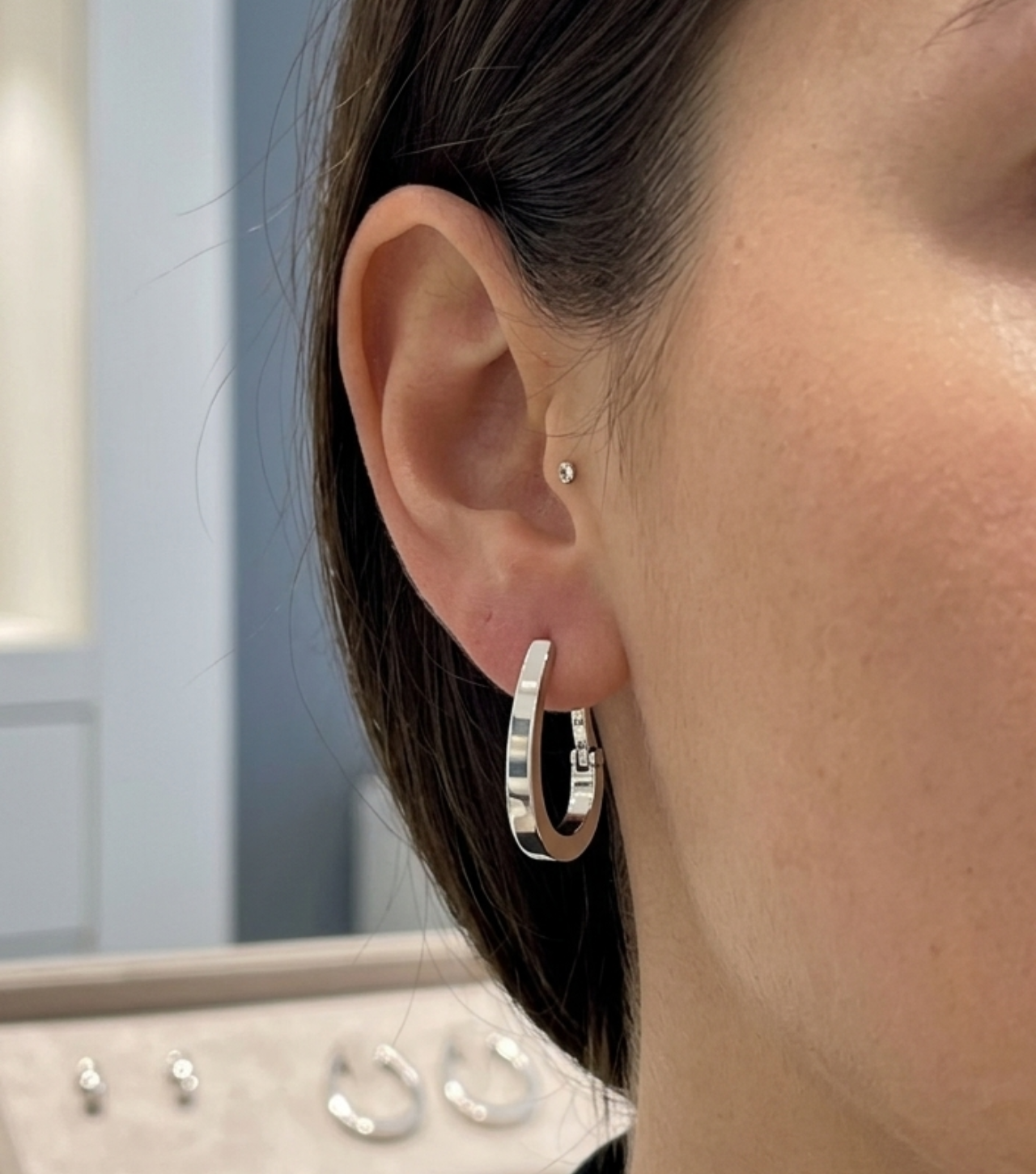 Créole ovale en or blanc non rhodié 18 carats portée au lobe d'une femme.
