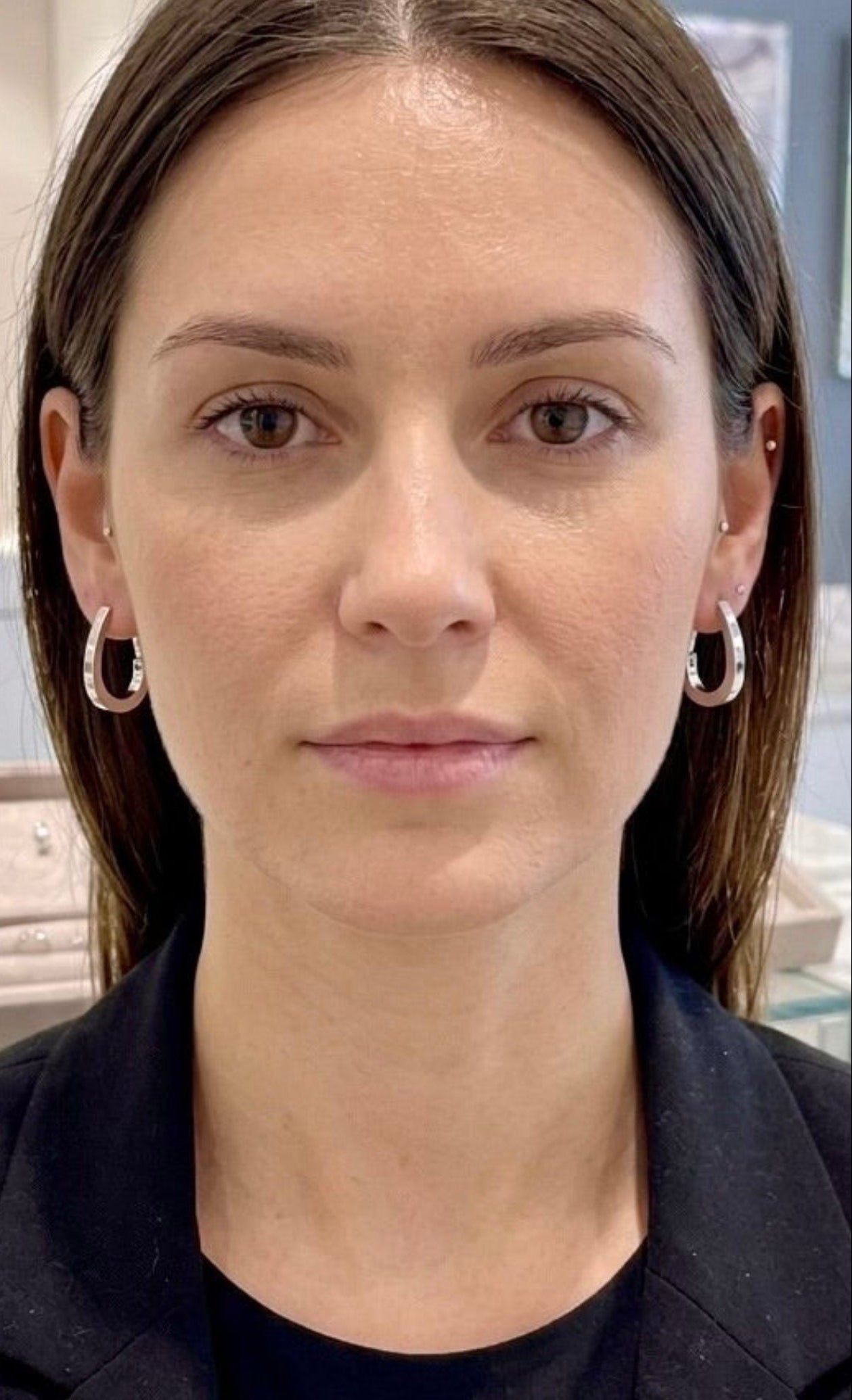 Boucles d'oreilles créoles ovales en or blanc 18 carats portées par une femme de face dans une bijouterie