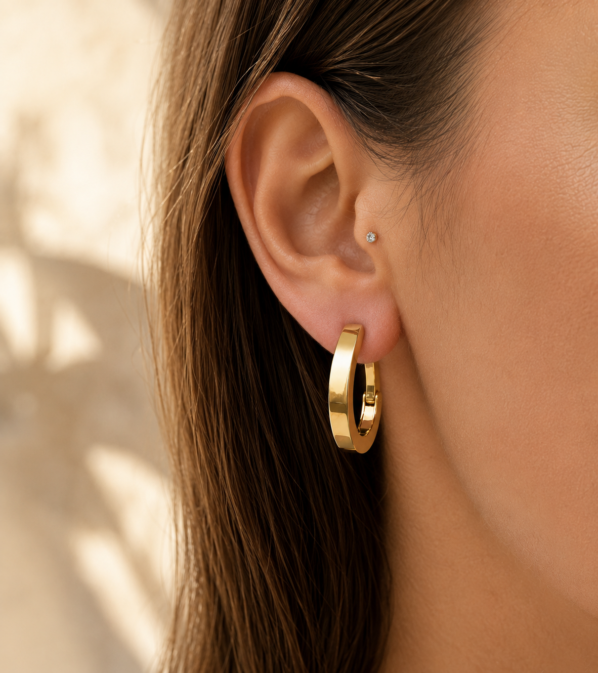 Créole ovale en or jaune 18 carats portée au lobe d'une femme.