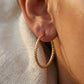 Créole torsadée en or jaune 18 carats de 30mm portée à l'oreille d'une femme au coucher du soleil.