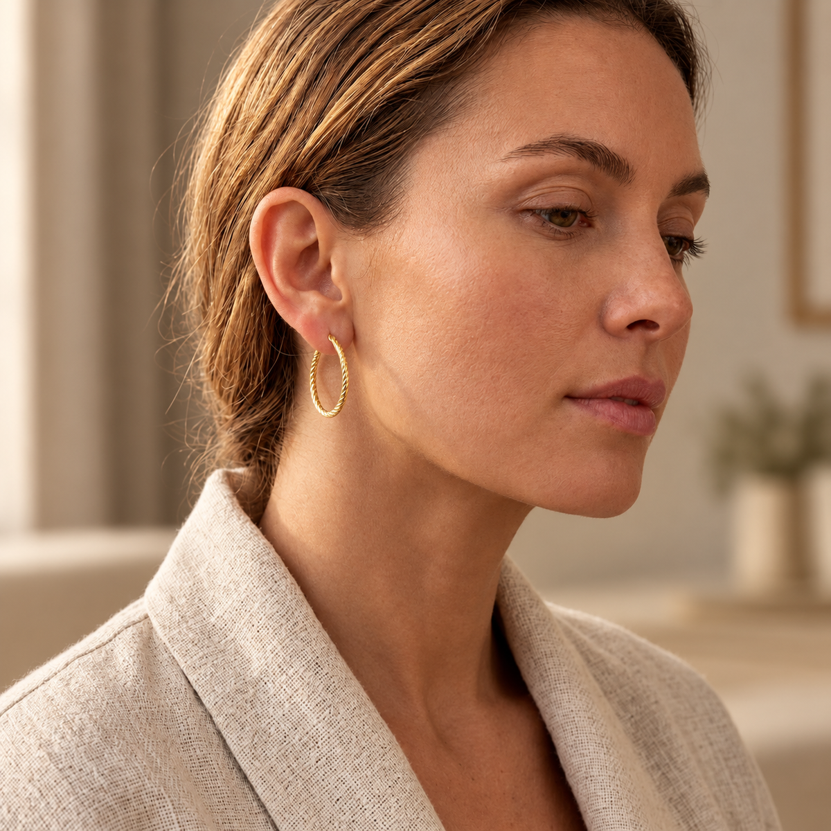Boucles d'oreilles créoles torsadées or 18 carats portées par une femme élégante de profil .