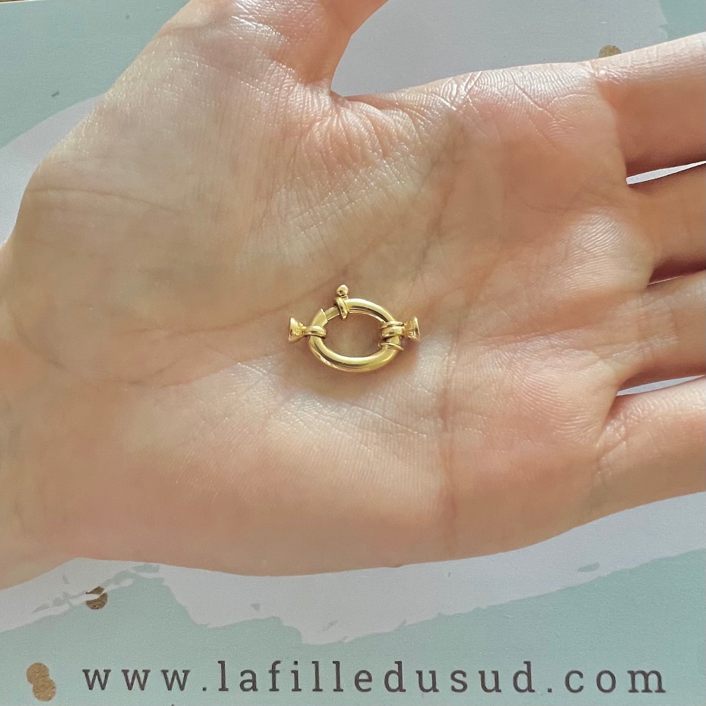 Aperçu de la taille réelle du fermoir bouée ovale en or 18 carats au creux d'une main.
