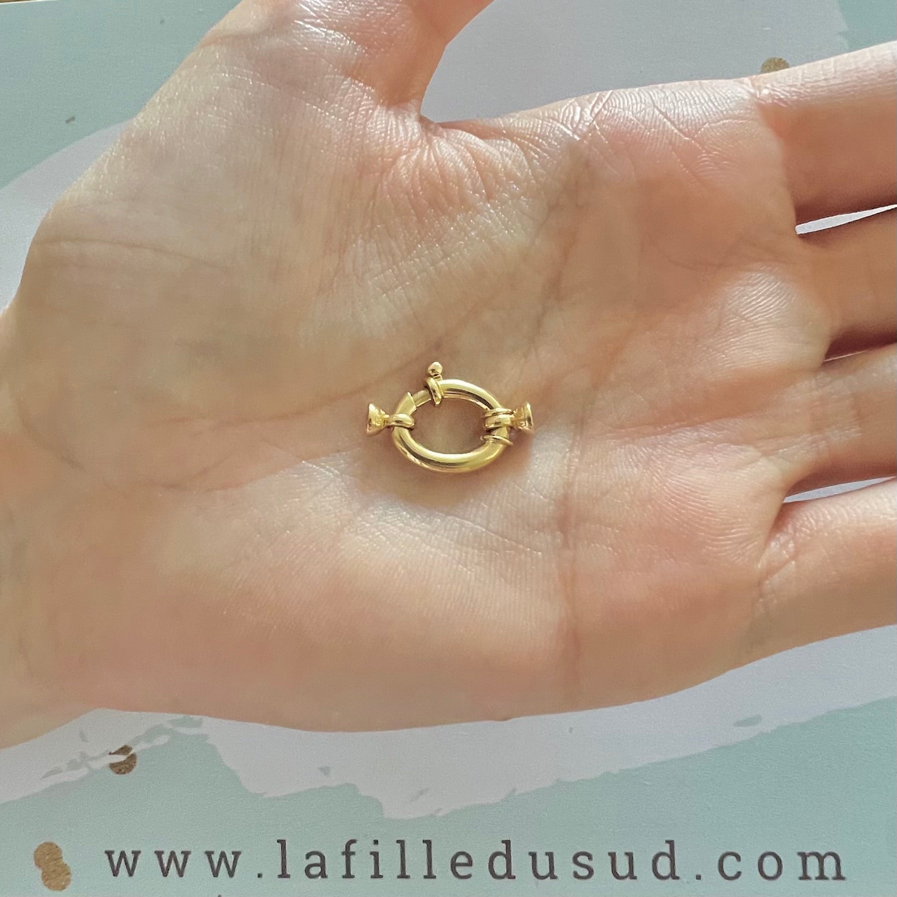 Aperçu de la taille réelle du fermoir bouée ovale en or 18 carats au creux d'une main.
