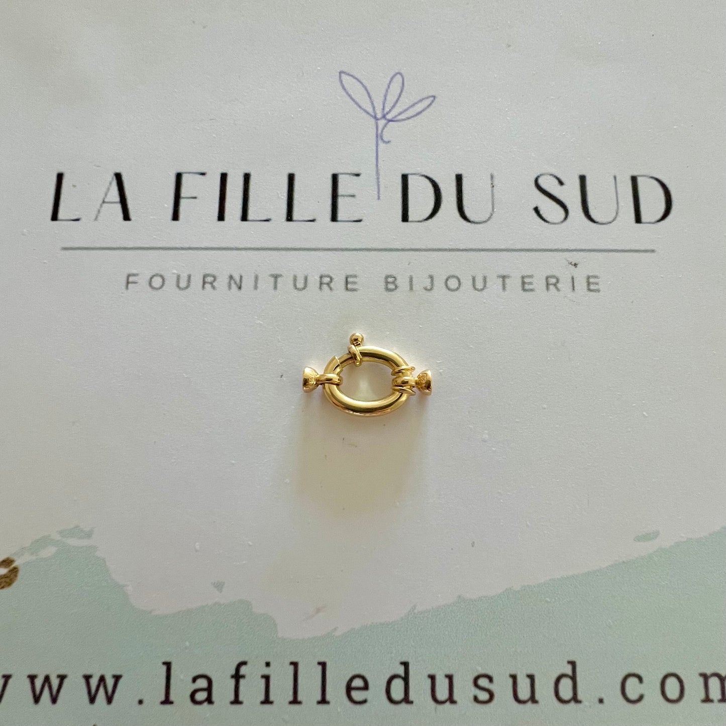 Fermoir bouée ovale en or 18 carats présenté sur la carte de l'atelier de fournitures de bijouterie.