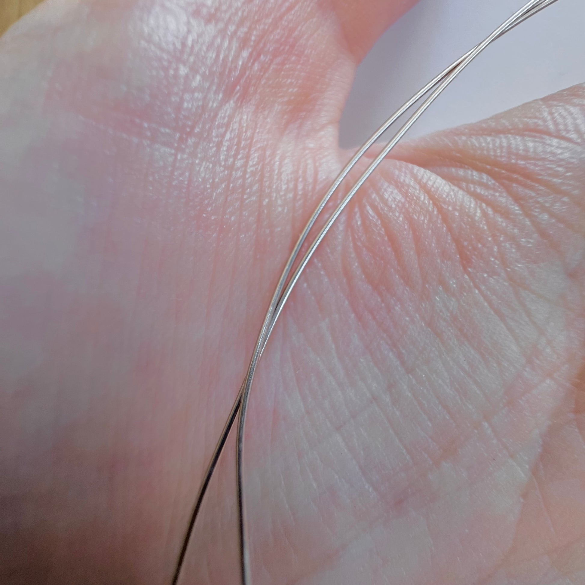 Macrophotographie montrant l'extrême finesse d'un demi-millimètre du fil d'or 18k sur la peau pour travaux de précision.