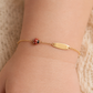 Gros plan sur le poignet d'un bébé portant une gourmette coccinelle rouge en or jaune 18 carats avec plaque ovale lisse.