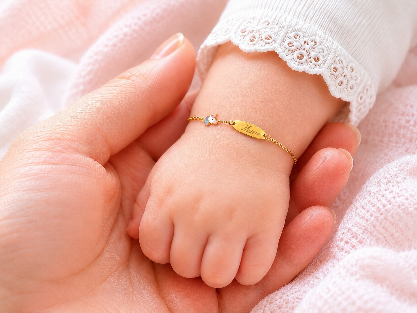 Poignet d'un bébé fille portant une gourmette en or jaune 18 carats avec une licorne et une gravure personnalisée 