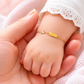 Gros plan d'un poignet de bébé fille portant une gourmette en or jaune 18 carats avec une plaque lisse et un motif licorne.