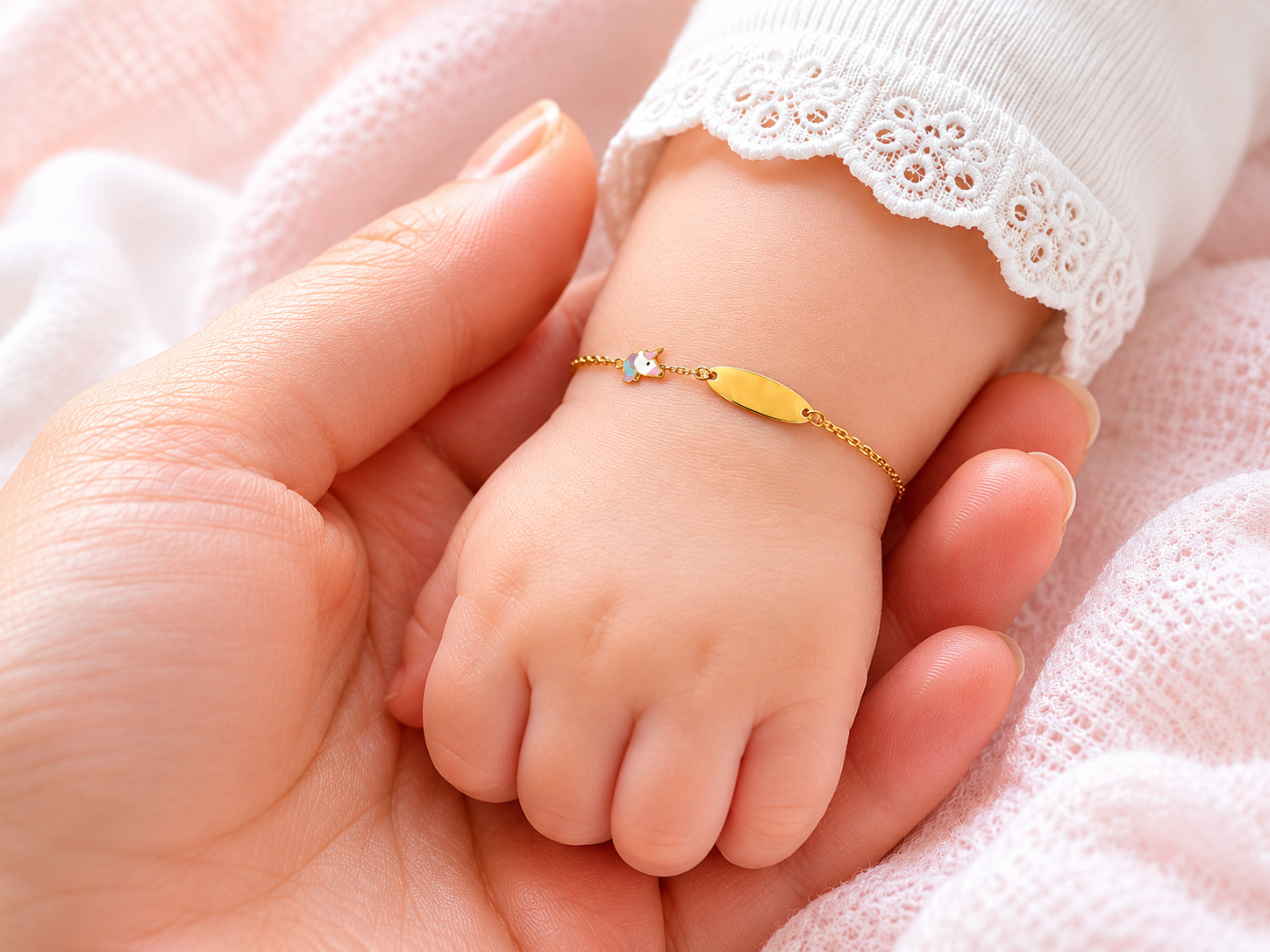 Gros plan d'un poignet de bébé fille portant une gourmette en or jaune 18 carats avec une plaque lisse et un motif licorne.