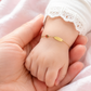Gros plan d'un poignet de bébé fille portant une gourmette en or jaune 18 carats avec une plaque lisse et un motif coccinelle.