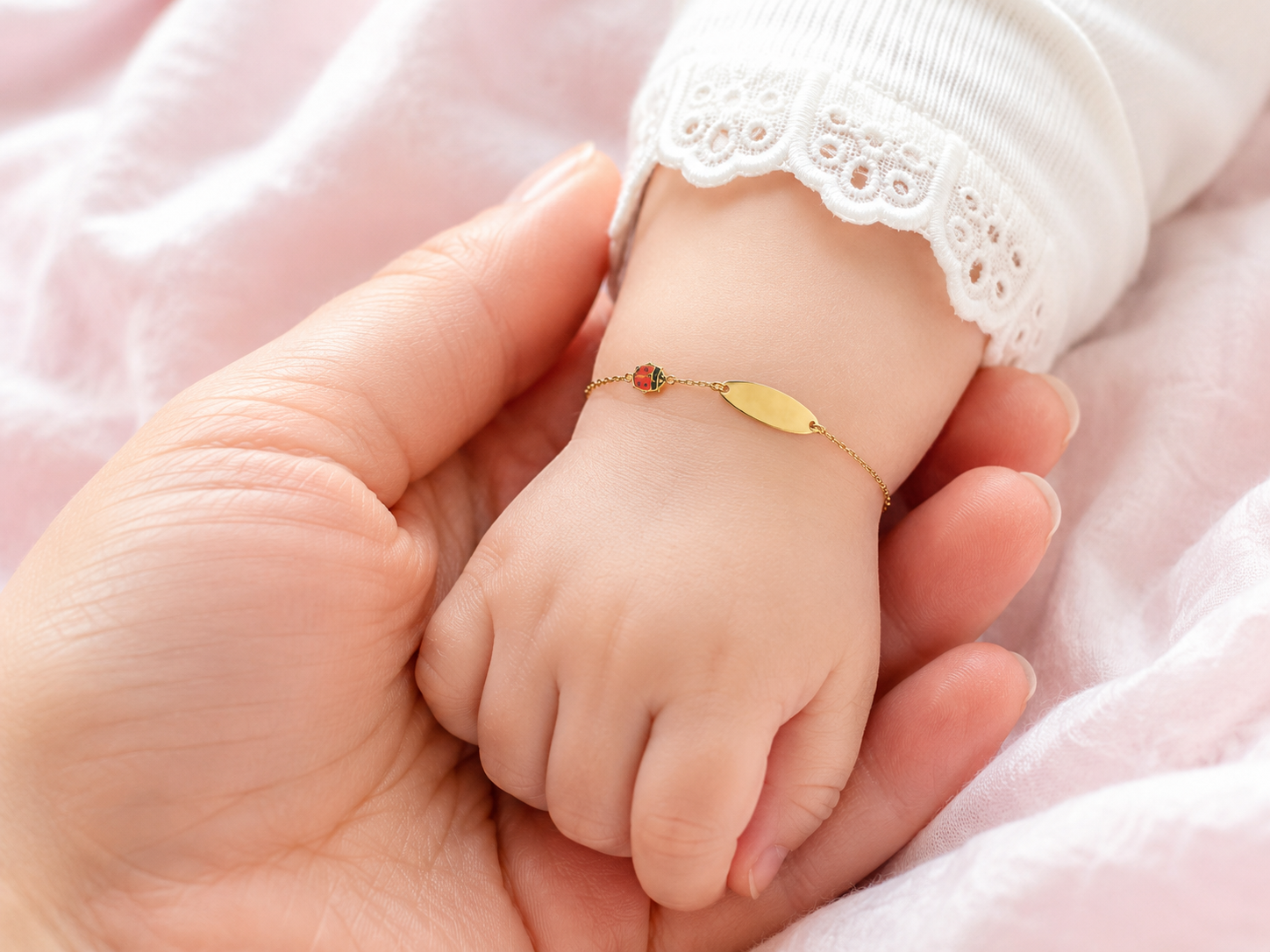 Gros plan d'un poignet de bébé fille portant une gourmette en or jaune 18 carats avec une plaque lisse et un motif coccinelle.