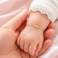 Gros plan d'un poignet de bébé fille portant une gourmette en or jaune 18 carats avec une plaque lisse et un motif fleur.