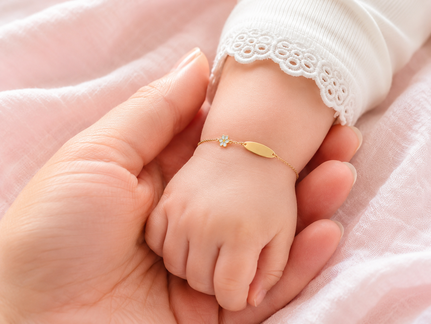 Gros plan d'un poignet de bébé fille portant une gourmette en or jaune 18 carats avec une plaque lisse et un motif fleur.