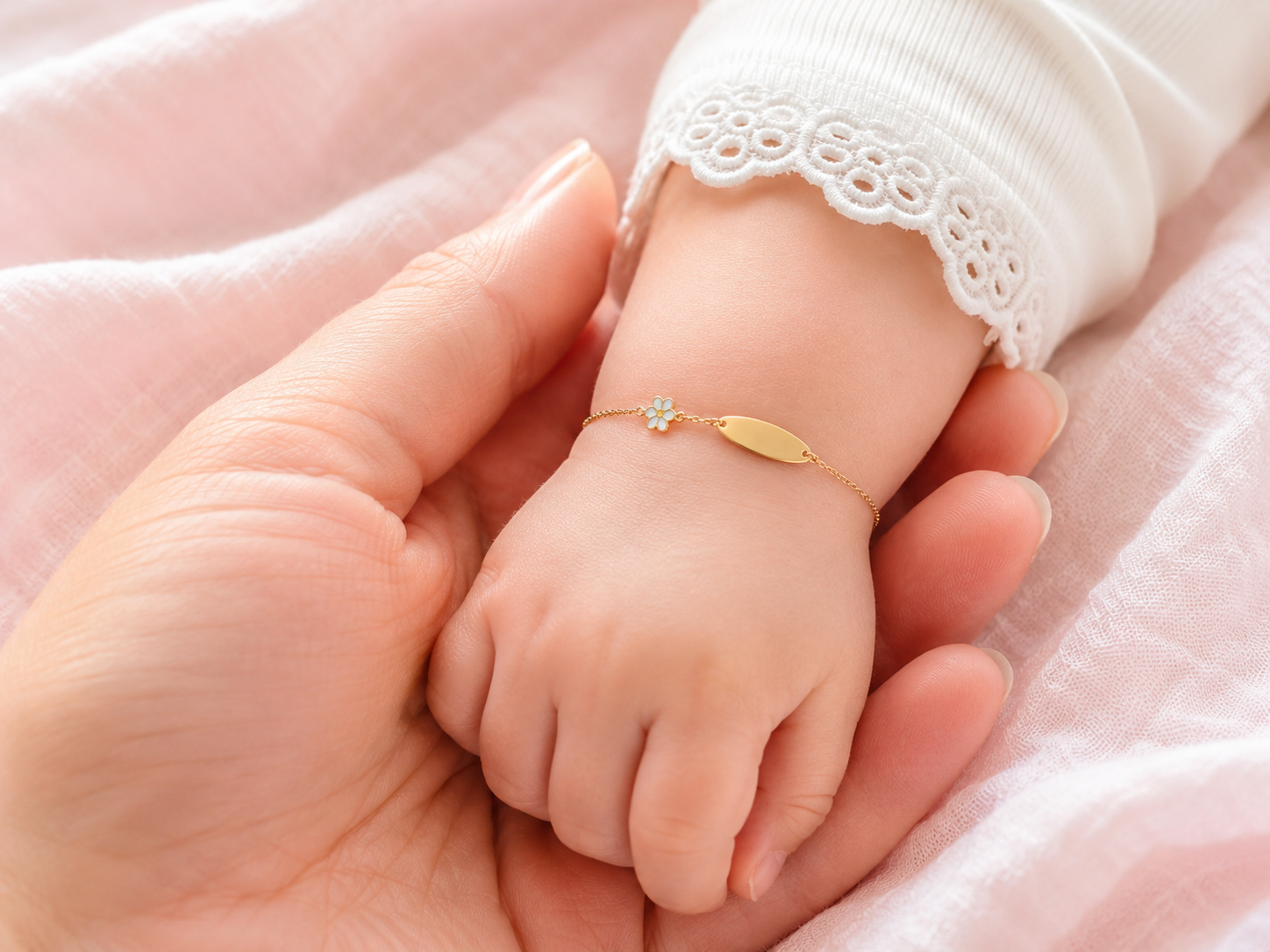 Gros plan d'un poignet de bébé fille portant une gourmette en or jaune 18 carats avec une plaque lisse et un motif fleur.
