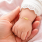 Gros plan d'un poignet de bébé fille portant une gourmette en or jaune 18 carats avec une plaque lisse et un motif papillon.