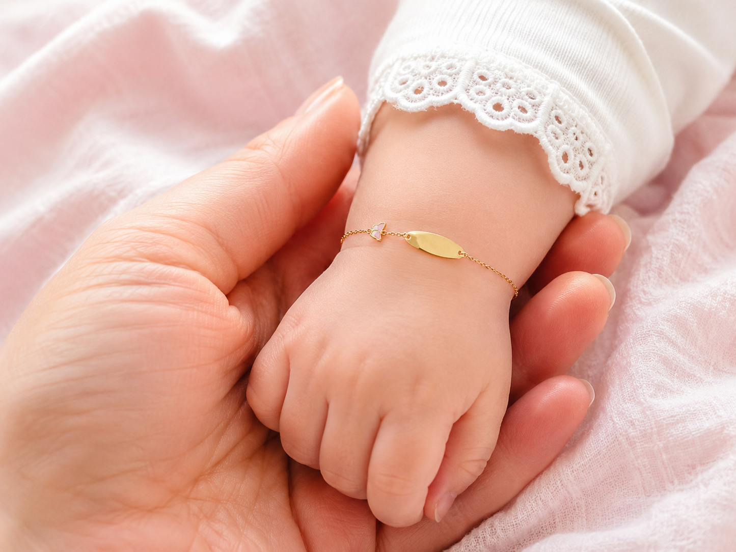 Gros plan d'un poignet de bébé fille portant une gourmette en or jaune 18 carats avec une plaque lisse et un motif papillon.