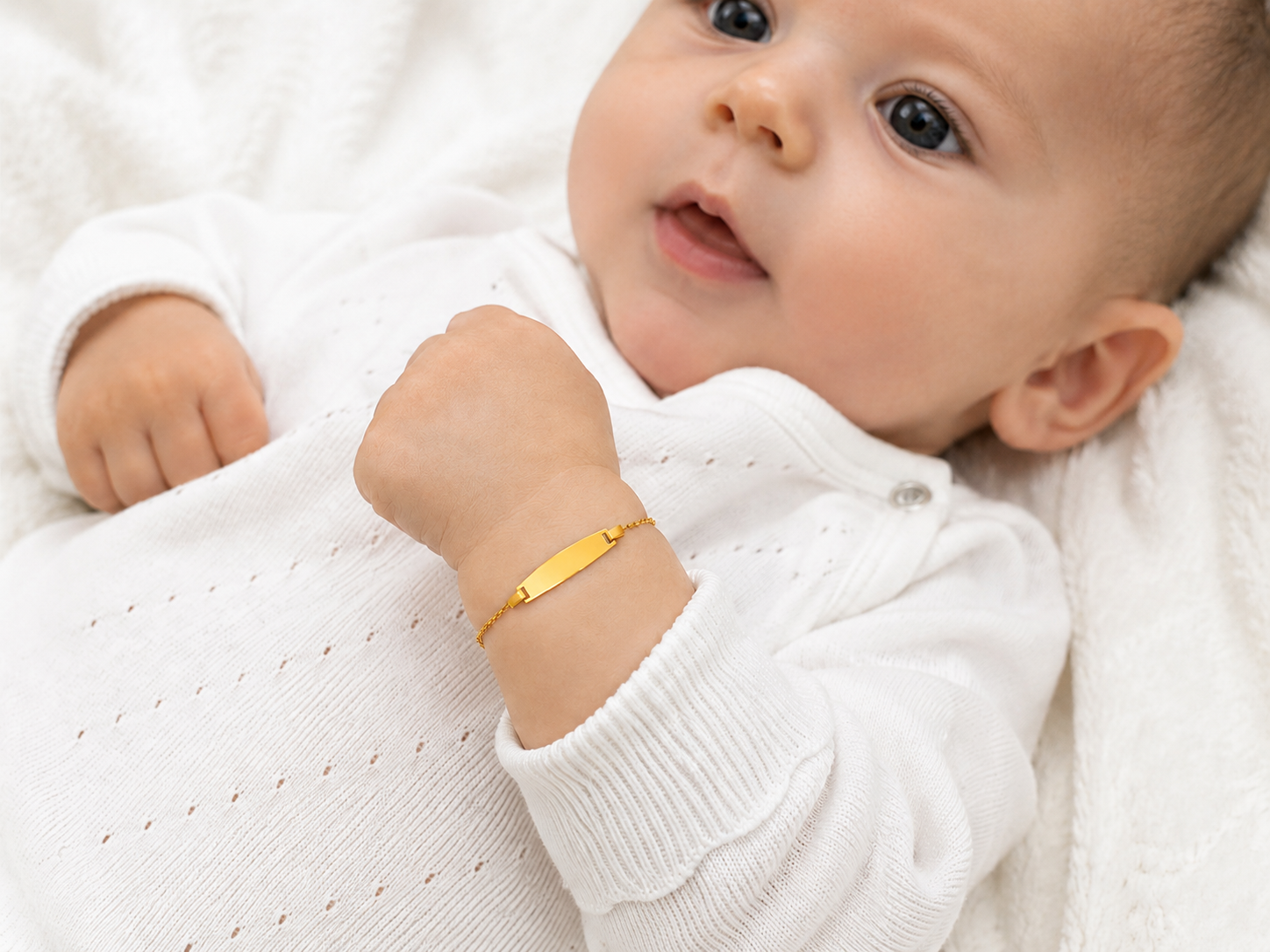 Bébé portant une gourmette de naissance en or jaune 18 carats avec plaque à graver.