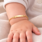 Bébé portant une gourmette de naissance en or jaune 18 carats avec plaque à graver.