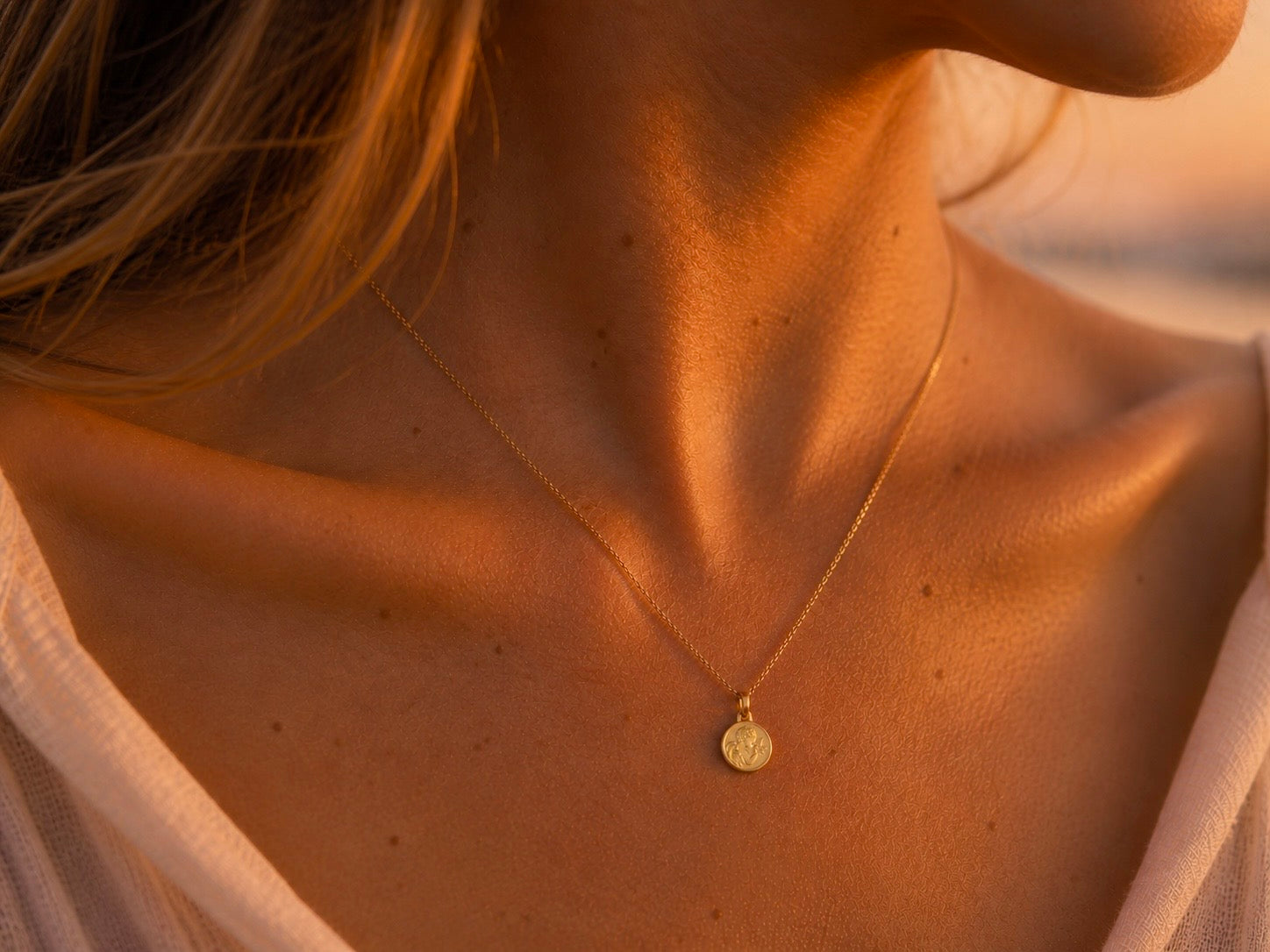 Gros plan sur le décolleté d'une femme portant la petite médaille de l'Ange à la Colombe en or jaune 18 carats, diamètre 14 mm, style bijou de peau.
