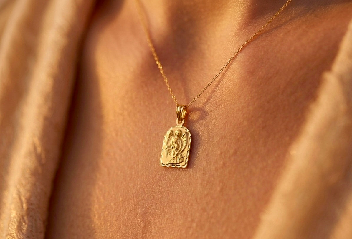 Gros plan sur le décolleté d'une femme portant la médaille de l'Ange Gardien en or jaune 18 carats, forme arche avec bords facettés et finition mate.