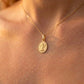 Gros plan sur le décolleté d'une femme portant la médaille ovale de l'Ange Priant en or jaune 18 carats, finition mate et bords facettés.