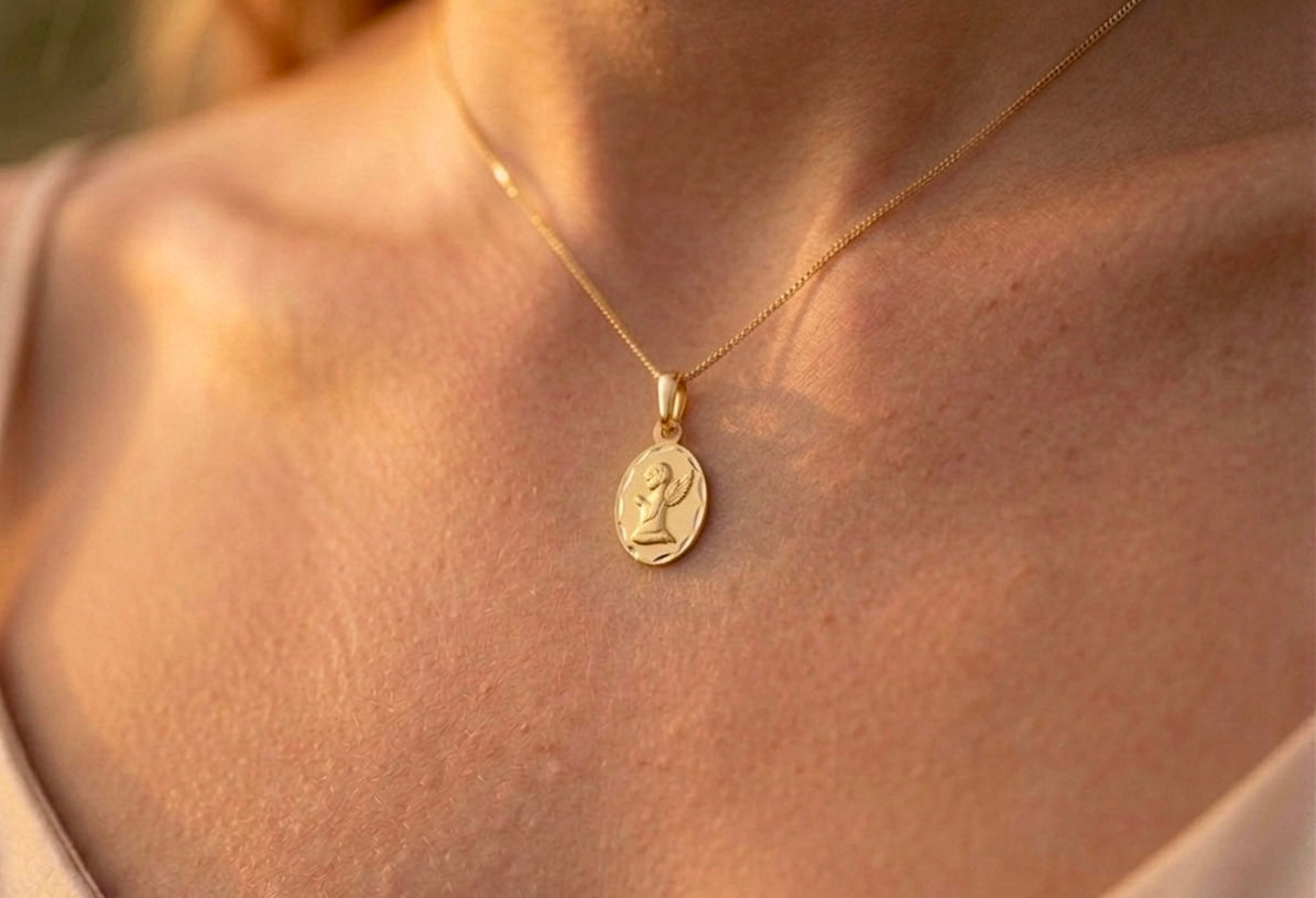 Gros plan sur le décolleté d'une femme portant la médaille ovale de l'Ange Priant en or jaune 18 carats, finition mate et bords facettés.