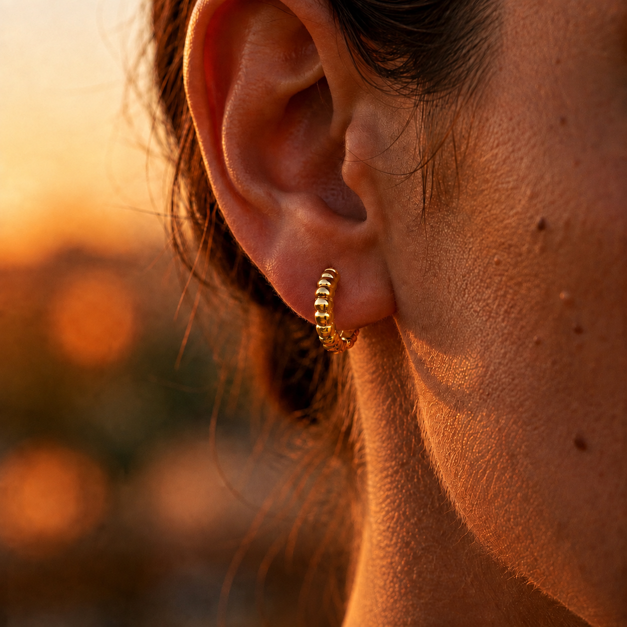 Petite créole épaisse et striée en or jaune 18 carats portée ajustée au lobe d'une femme au soleil.