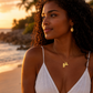 Pendentif carte de la Guadeloupe en or jaune 18 carats porté par une femme à la plage au coucher du soleil.