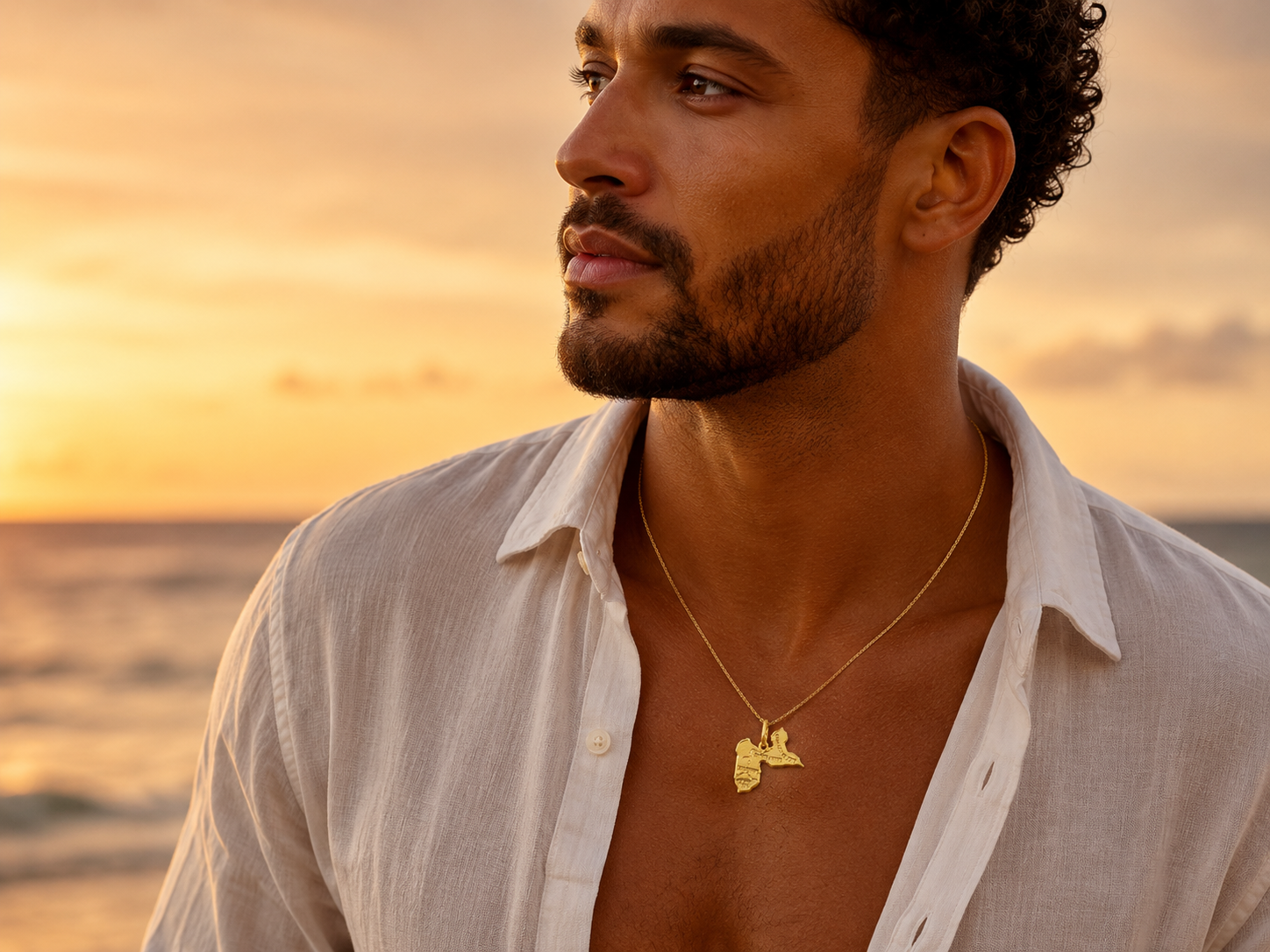Collier carte de la Guadeloupe en or jaune 18 carats porté par un homme à la peau dorée au coucher du soleil.