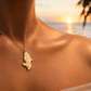 Pendentif en or jaune 18 carats en forme de carte de la Martinique porté au cou d'une femme au coucher du soleil.