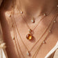 Gros plan sur une femme portant un pendentif en or jaune 18 carats serti d'une citrine naturelle taille cabochon, porté en accumulation avec d'autres chaînes fines.
