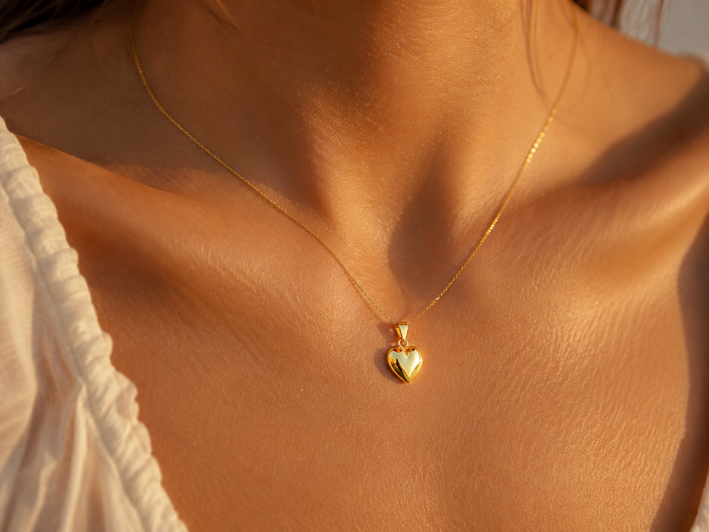 Gros plan sur le décolleté d'une femme portant un petit pendentif cœur bombé en or jaune 18 carats, bijou de peau minimaliste et brillant.