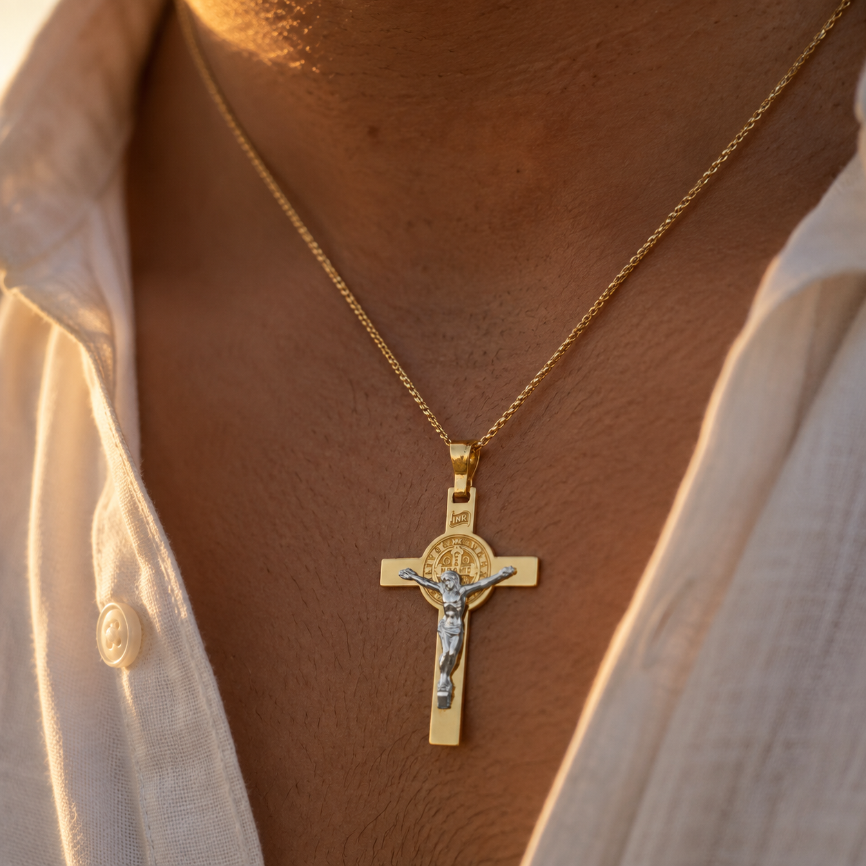 Pendentif croix de protection Saint Benoît en or jaune et blanc 18 carats porté au cou sur une chaîne fine.