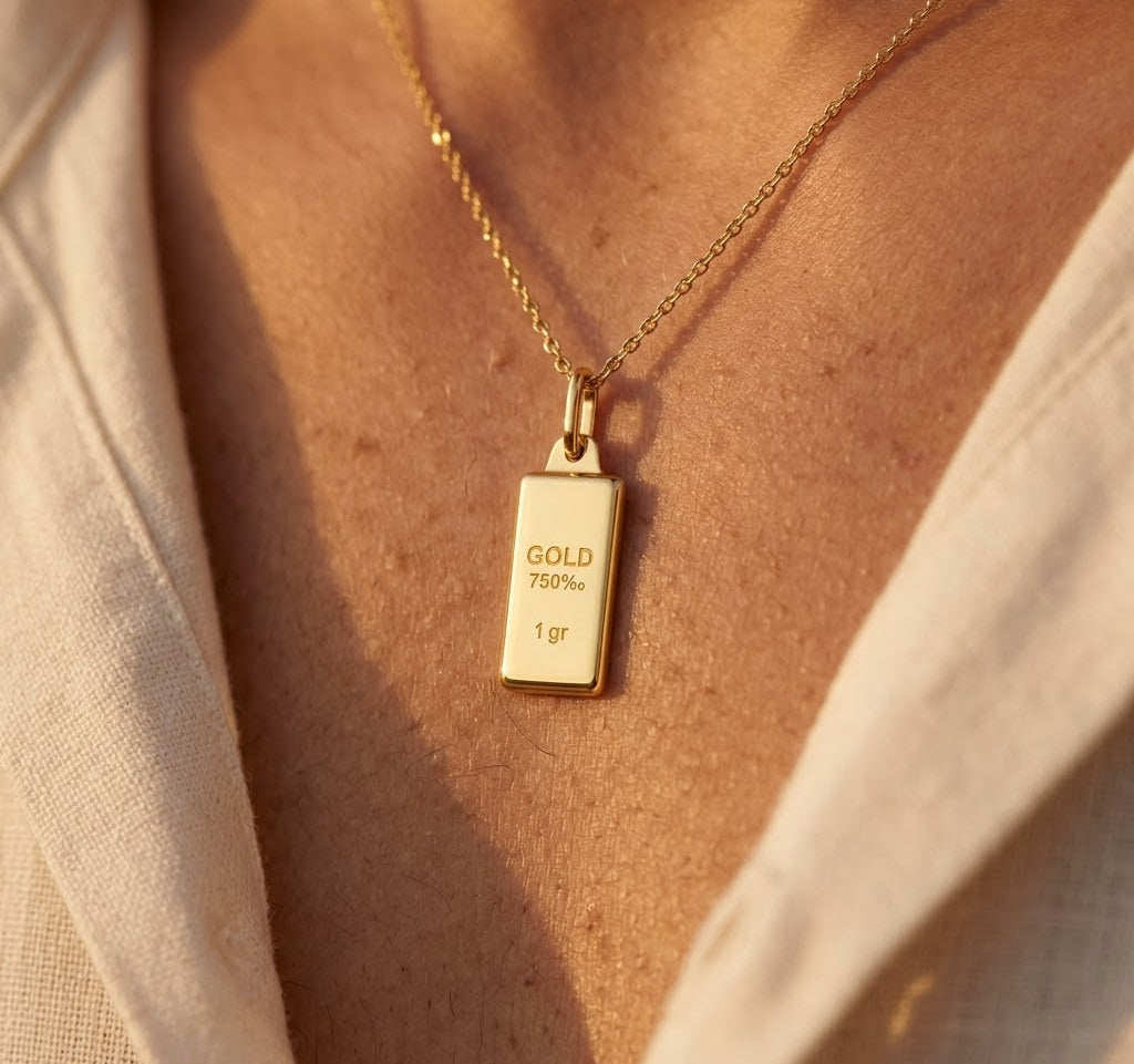 Pendentif lingot d'or 18 carats massif de 1 gramme porté sur une chaîne en or au coucher du soleil.
