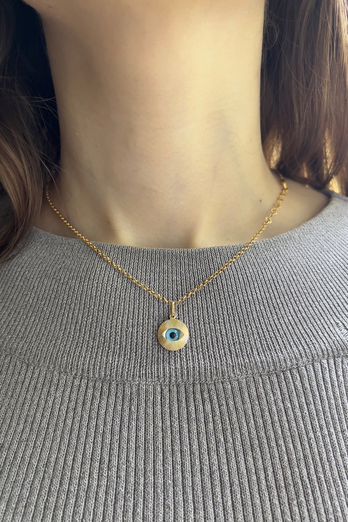  Femme portant un collier avec oeil bleu protecteur en or 18 carats sur une chaîne fine, style ras-de-cou élégant.