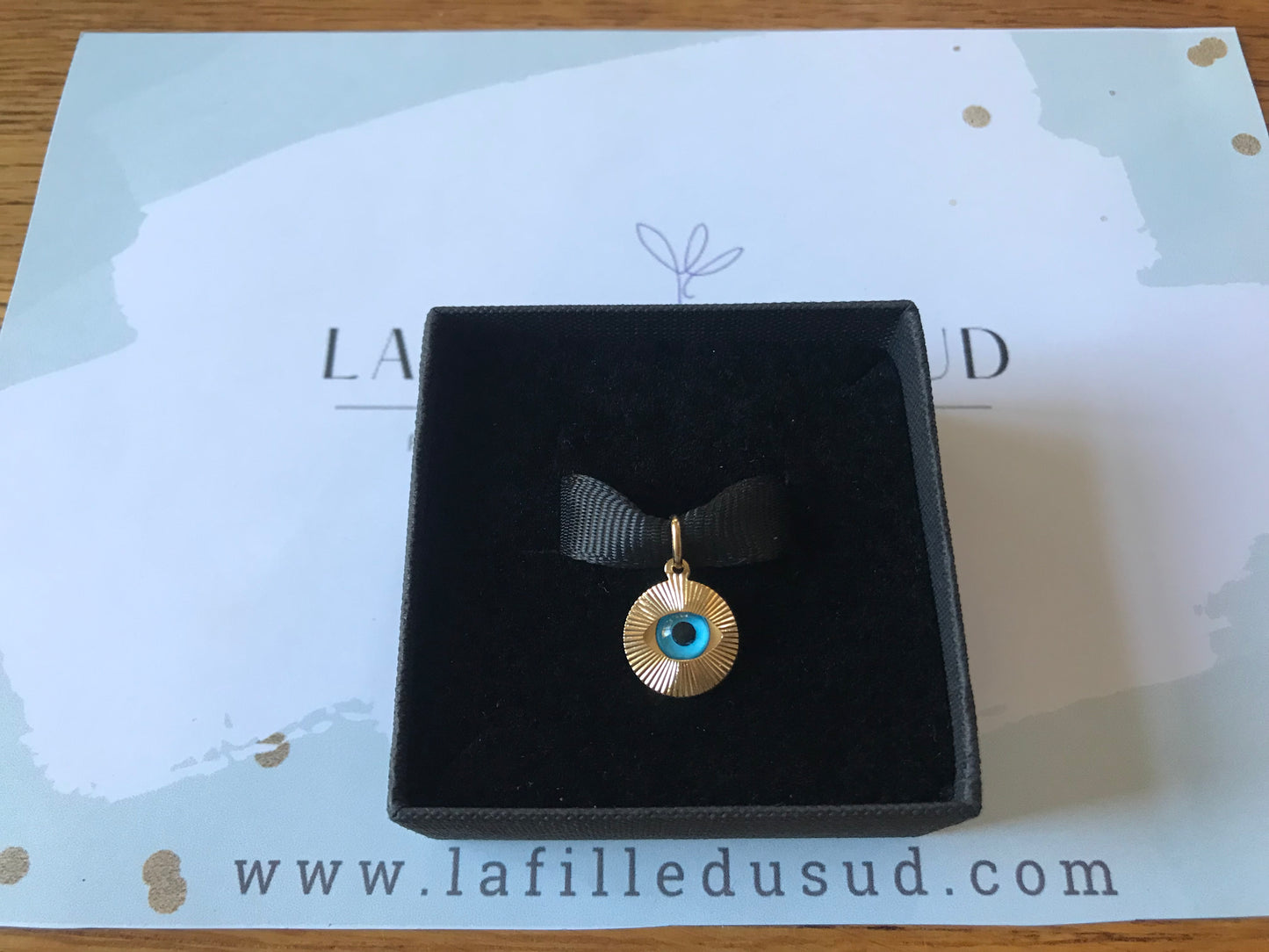 Idée cadeau : pendentif or oeil bleu présenté dans sa boîte à bijoux noire, prêt à offrir avec signification de protection.