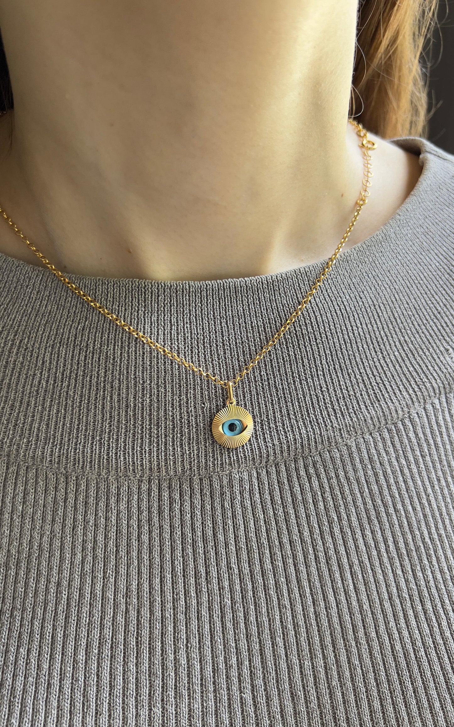  Femme portant un collier avec oeil bleu protecteur en or 18 carats sur une chaîne fine, style ras-de-cou élégant.