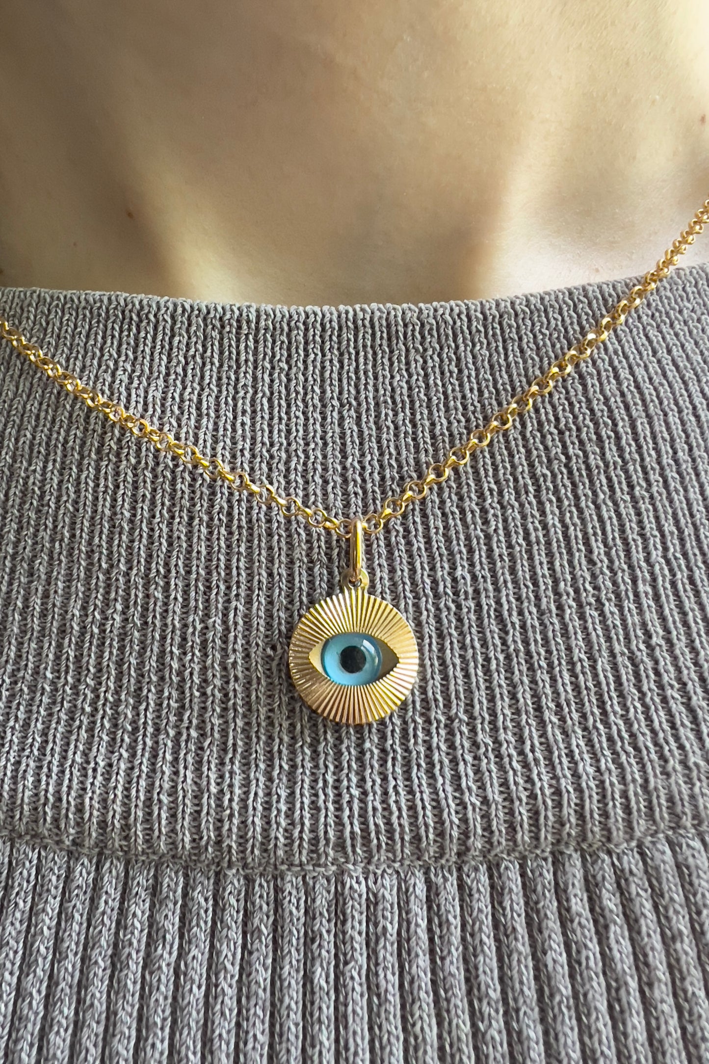  Femme portant un collier avec oeil bleu protecteur en or 18 carats sur une chaîne fine, style ras-de-cou élégant.