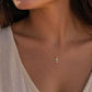 Gros plan sur le décolleté d'une femme portant la petite croix diamant en or 18k au soleil couchant.