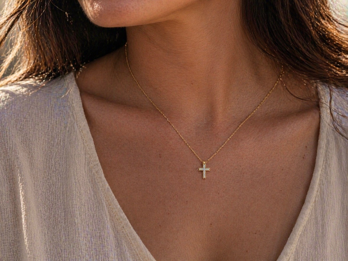 Gros plan sur le décolleté d'une femme portant la petite croix diamant en or 18k au soleil couchant.