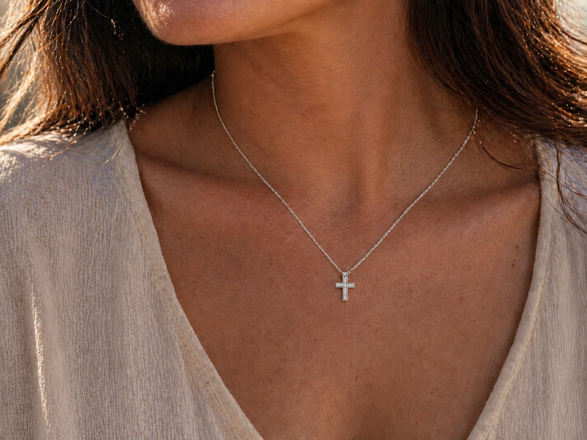 Femme portant la petite croix diamant en or blanc 18k au soleil couchant.