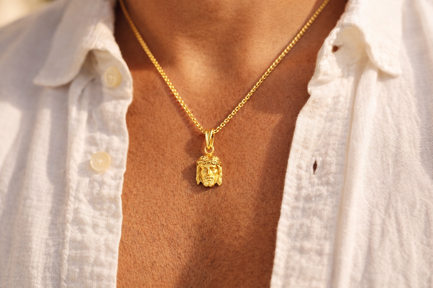 Torse d'un homme portant un pendentif tête de Christ en or jaune 18 carats sur une chaîne, le visage de Jésus contraste élégamment sur la peau bronzée.