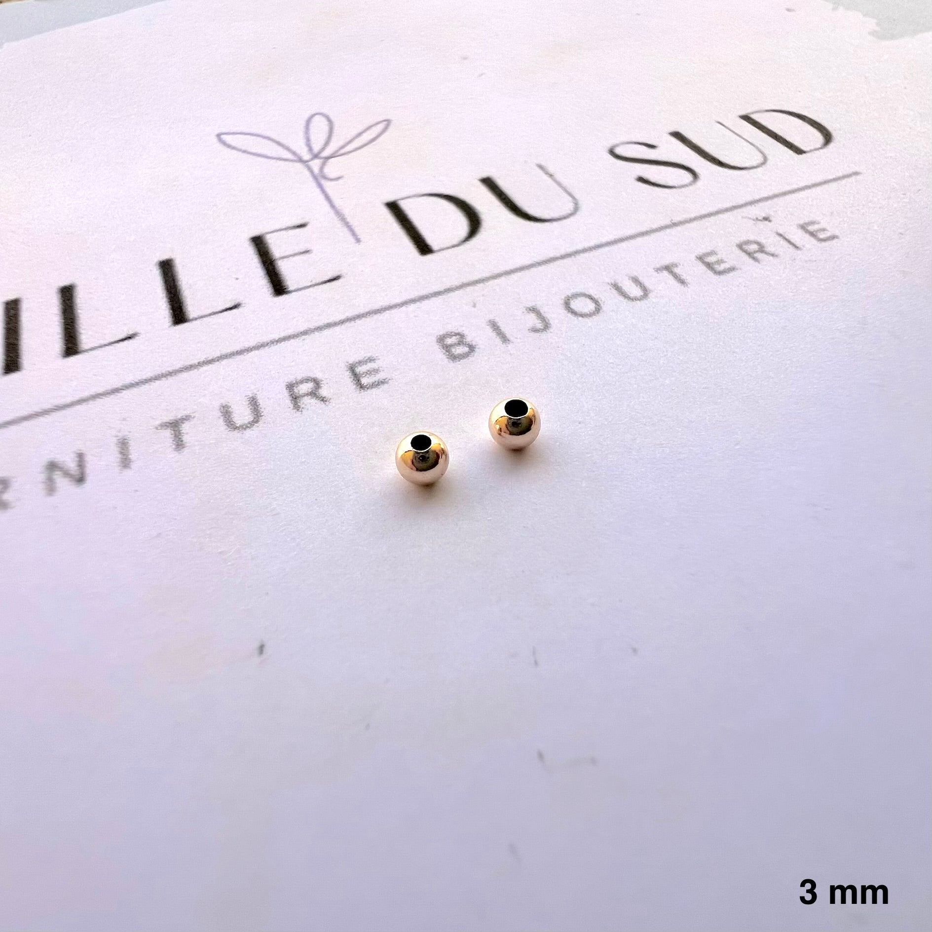 Perles boules lisses en or jaune 375 millièmes de 3 mm présentées sur la carte de l'atelier.