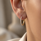 Petite créole or jaune et diamants 18 carats portée ajustée au lobe d'une femme sous une lumière solaire chaleureuse.