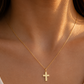 Pendentif petite croix plate en or jaune 18 carats porté au cou d'une femme sur une chaîne fine.